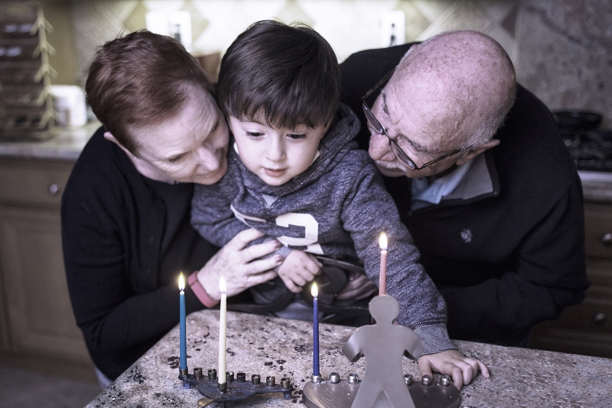 Jewish grandparents lighting the menorah with grandchild