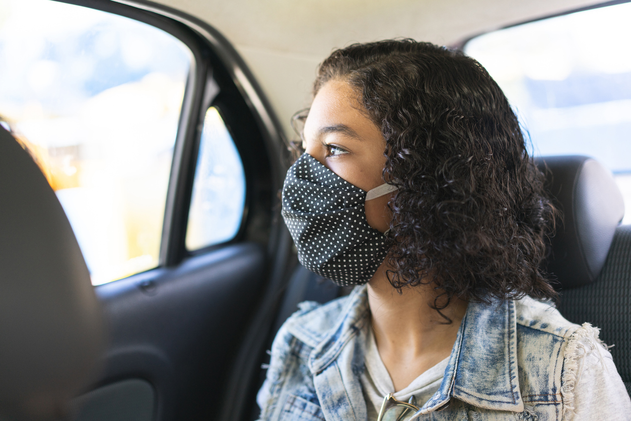 A young woman wearing a face mask in the back seat of a car