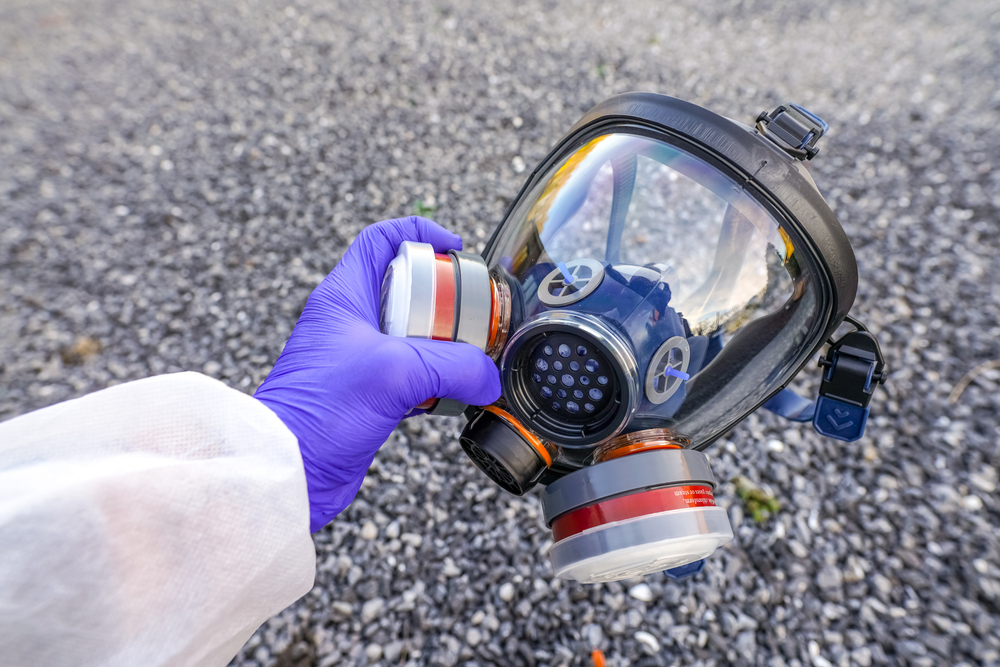 A purple gloved hand holding a full face elastomeric face mask