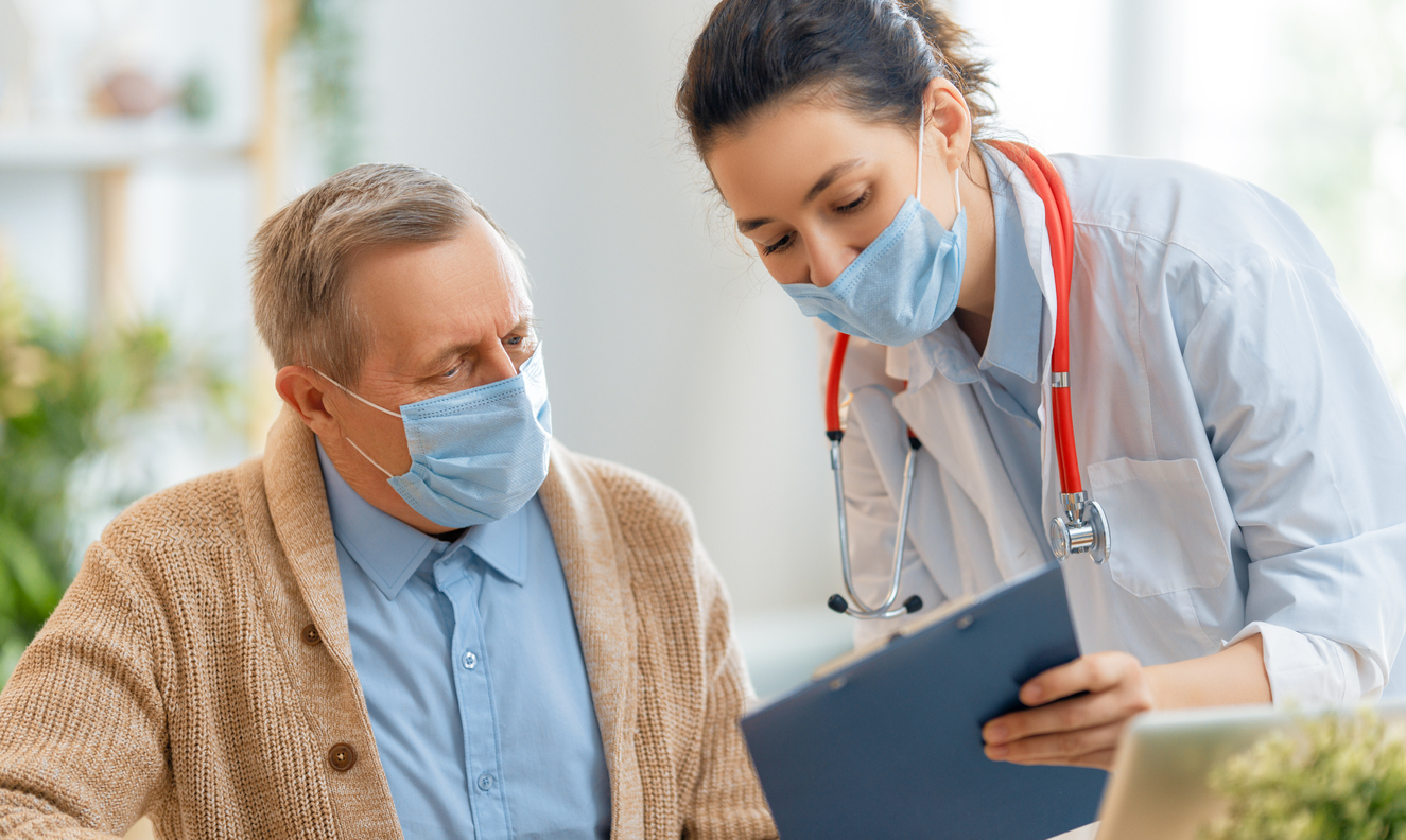 A senior man wearing a face mask speaks with a female healthcare worker, who is also wearing a face mask