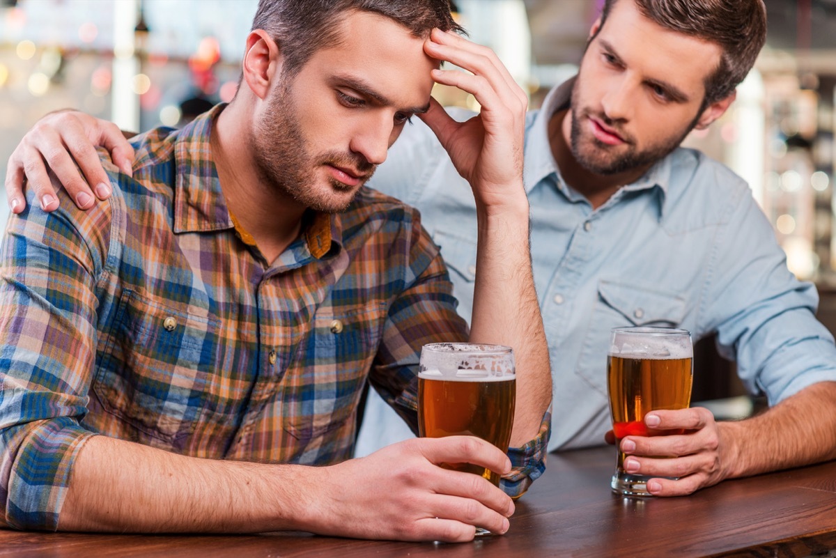 white man putting his arm around other white man while they drink beers