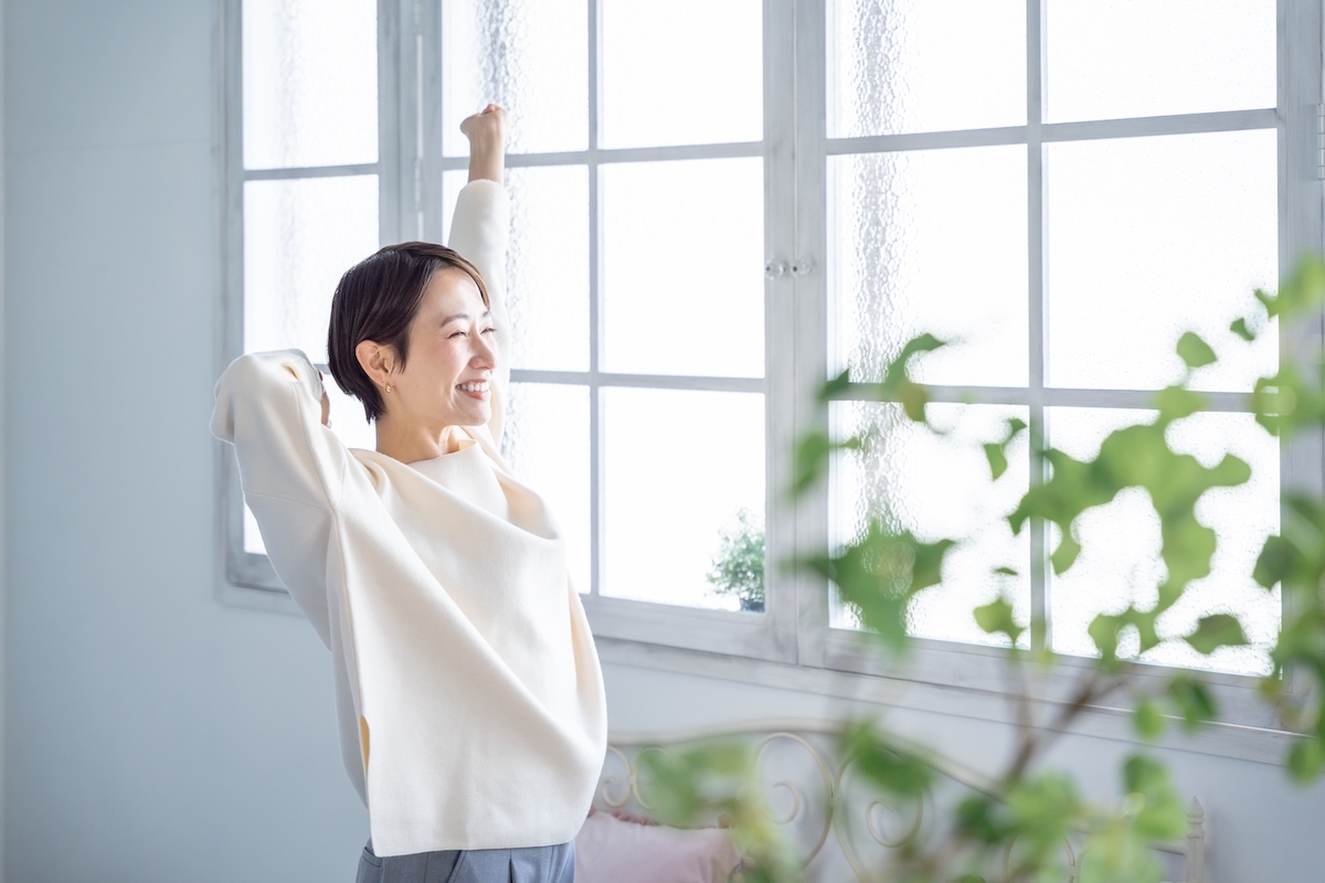 A woman dressed in white stretching and smiling in front of a large window