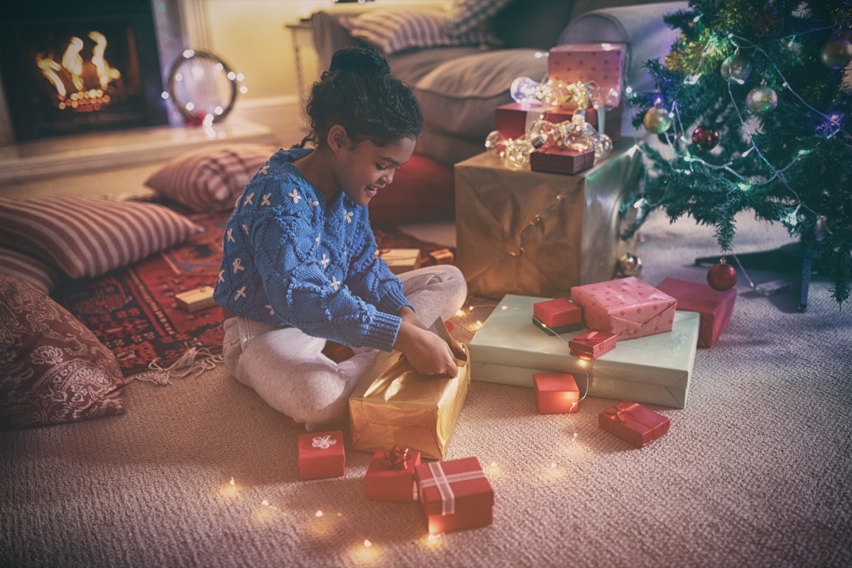 little girl unwrapping gifts in front of the fireplace on christmas morning