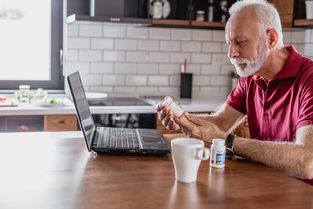 Senior man is looking for information about the medicine over the Internet. He is holding a medicine in one hand