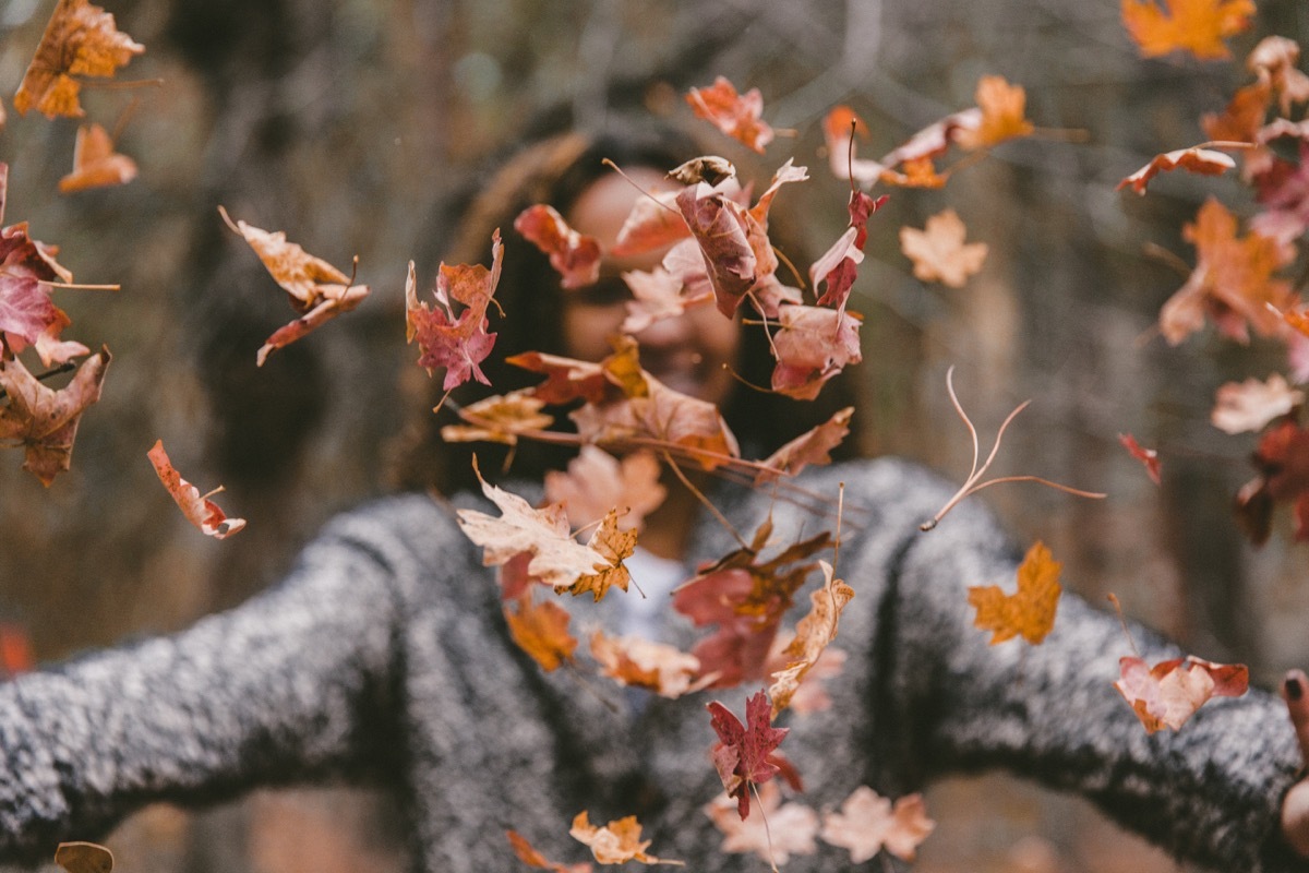 Woman throwing crunchy fall leaves in the air fall weather health