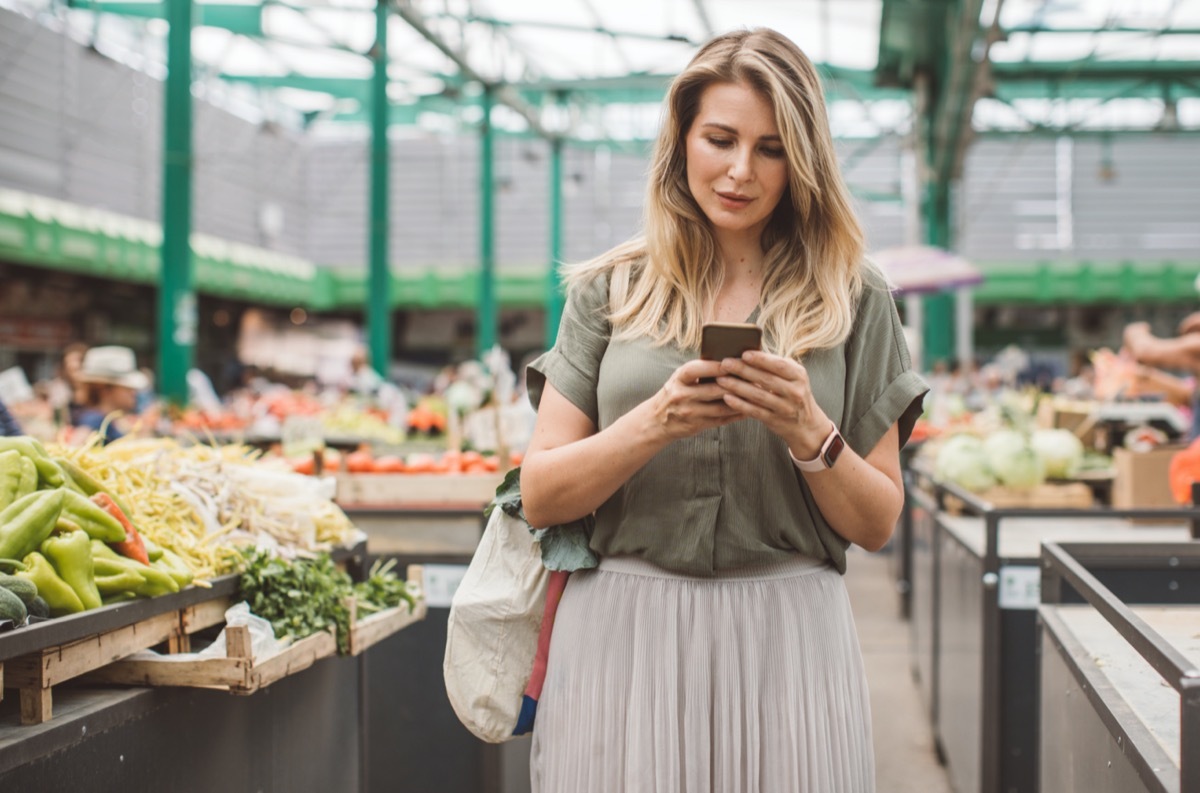 Cheerful woman selecting fresh vegetables in market, everything is fresh and organic. She using mobile phone to check is everything purchased