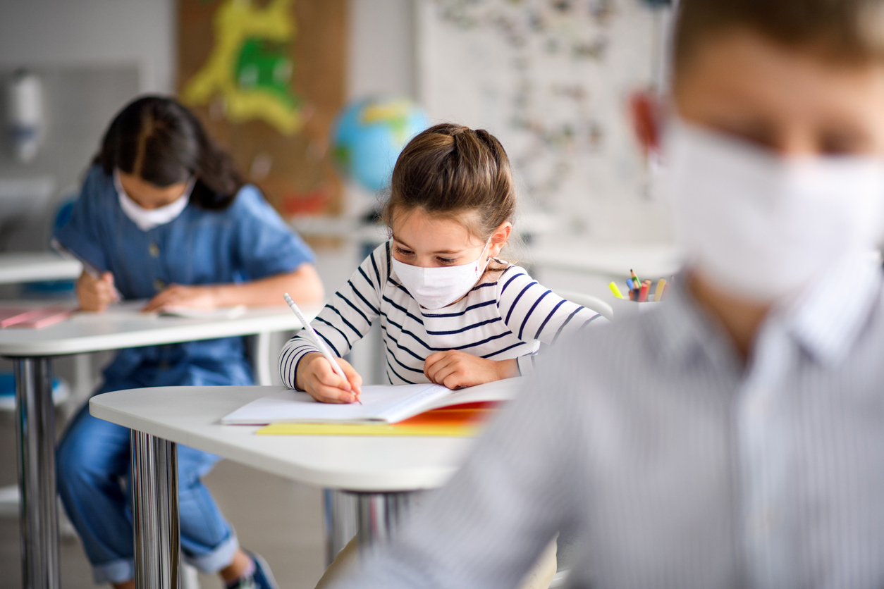 Children in a classroom wearing face masks and writing in notebooks.