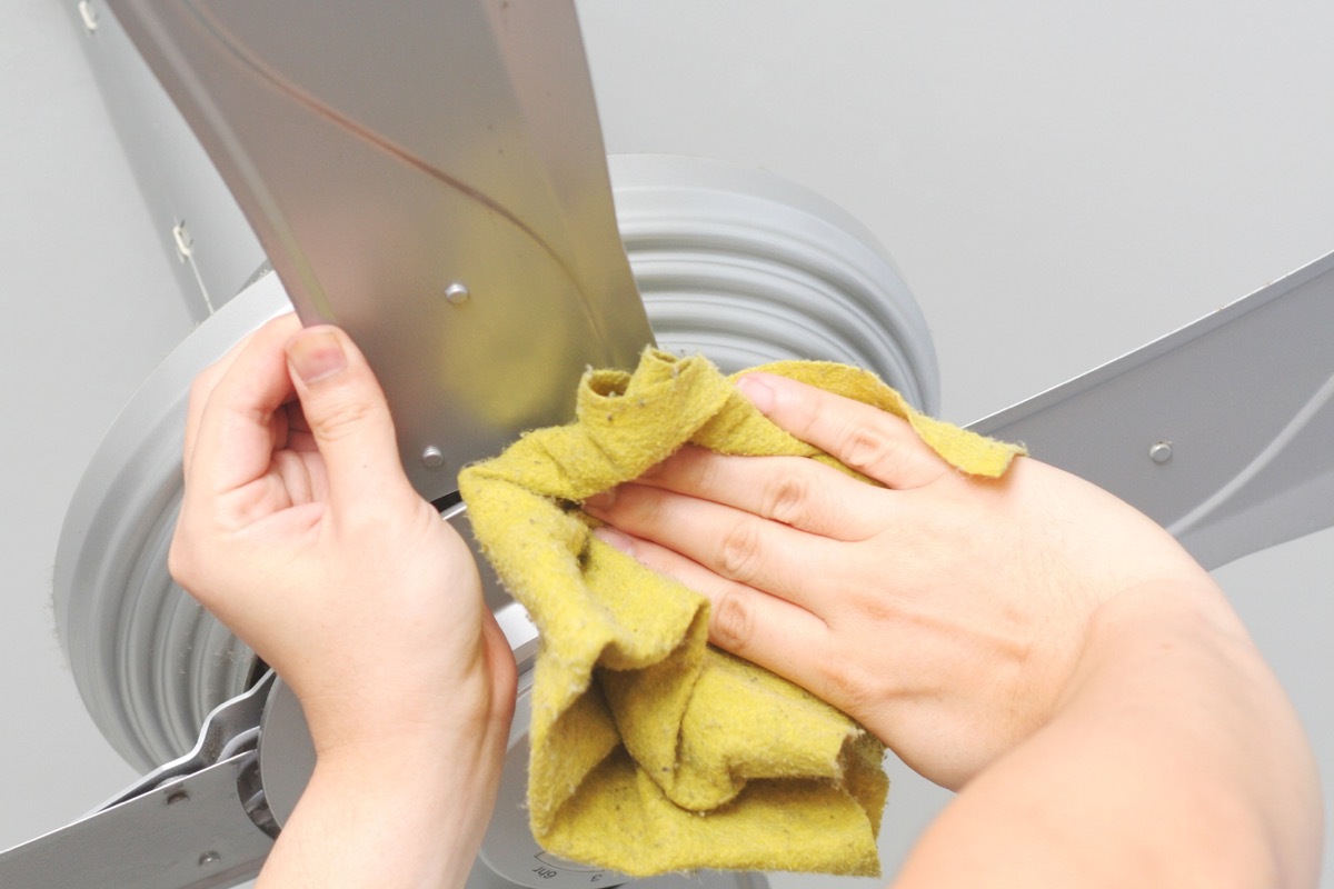 close up of hands wiping down ceiling fan