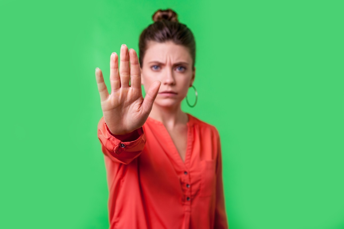 Stop, no! Portrait of angry or worried young woman with bun hairstyle, big earrings and in red blouse frowning gesturing caution to camera, prohibition. indoor studio shot isolated on green background (Stop, no! Portrait of angry or worried young woma