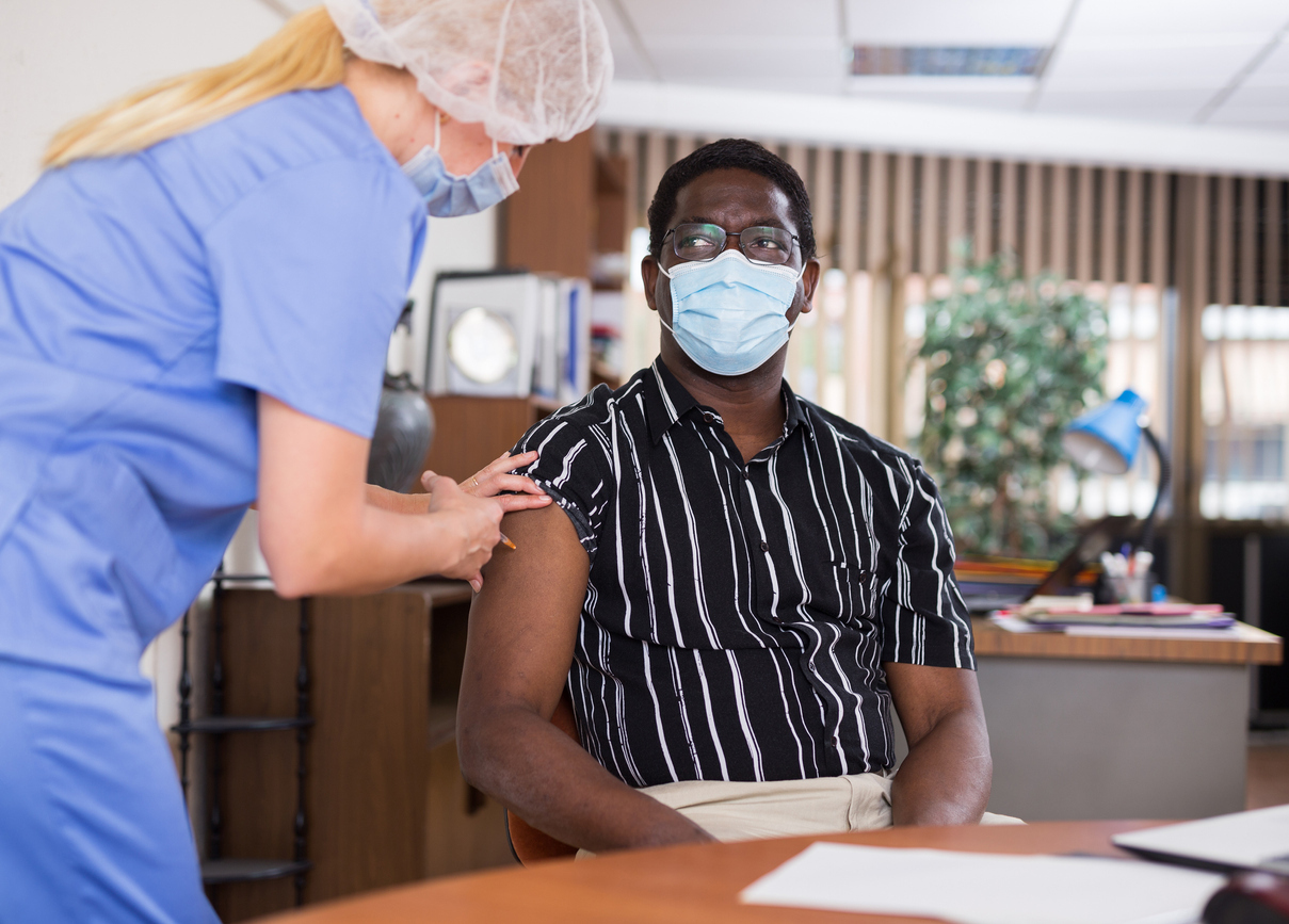 A young man wearing a face mask receives a COVID-19 vaccine from a healthcare worker