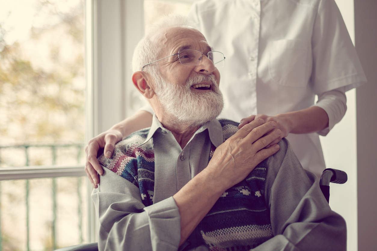 Senior man sitting in a wheelchair, laughing and holding his nurse's hand