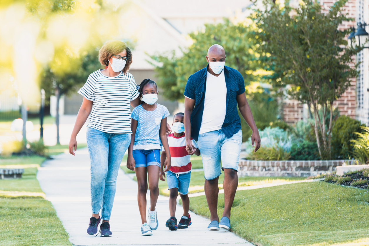 A family of four walking on a sidewalk while wearing face masks.