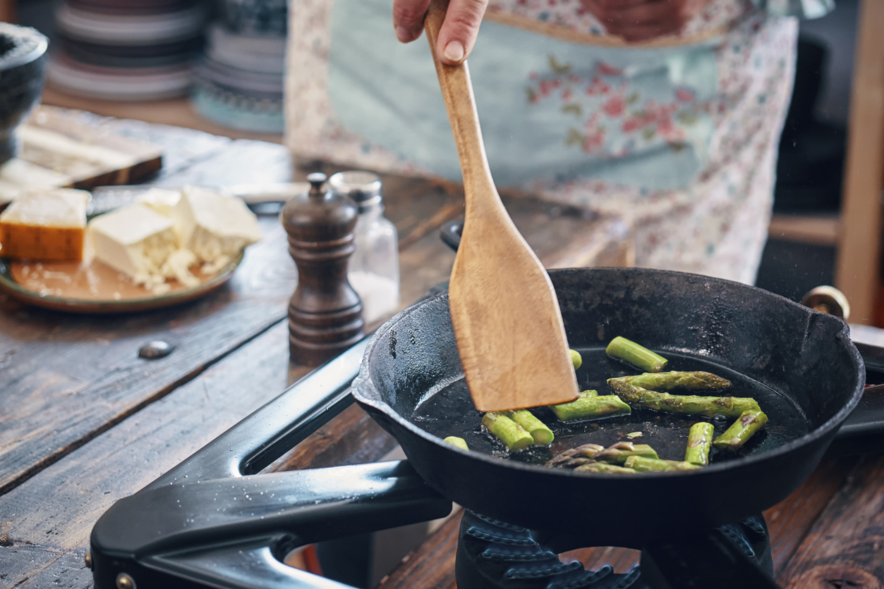 A close up of someone cooking asparagus in a cast iron skillet.