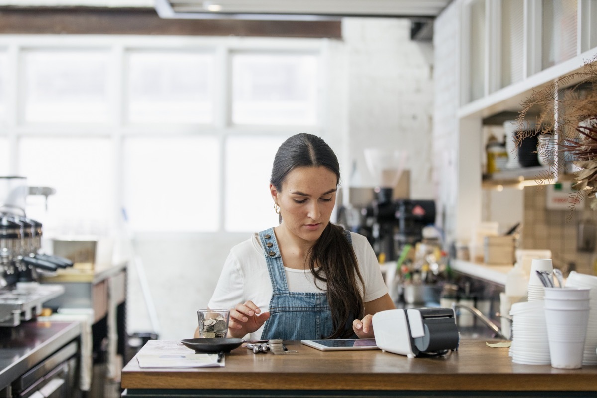 A front view shot of a waitress handling money behind a counter in a cafe.