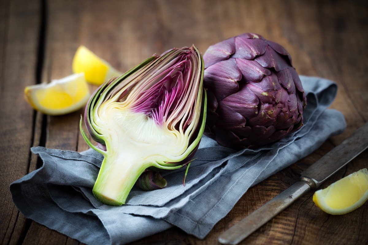 Fresh purple artichokes on dark rustic wooden background with slices of lemon