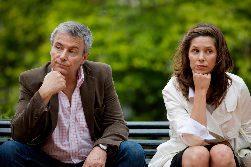 Unhappy middle-aged distanced couple on bench