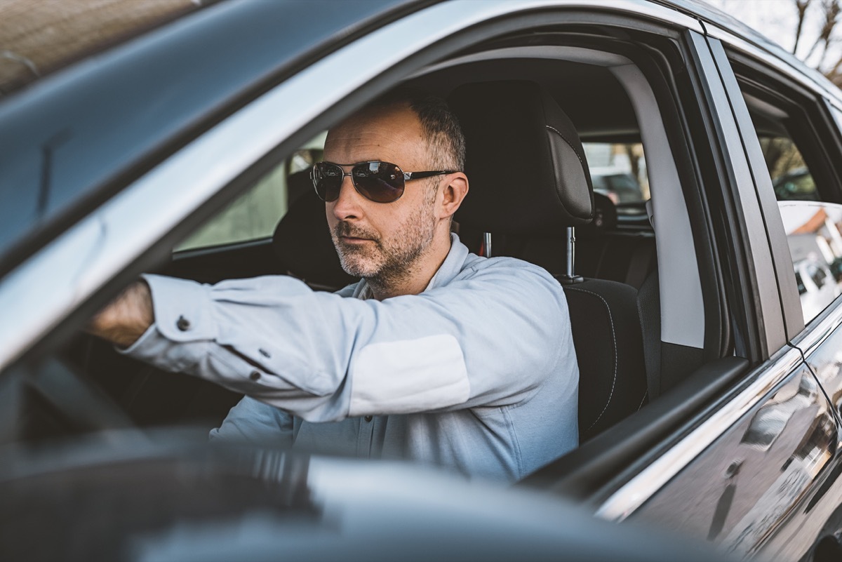 Businessman driving a car with sunglasses on and windows down.