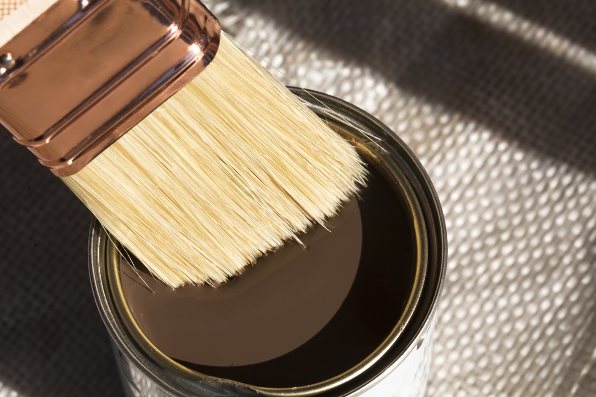 close up of a can of brown paint and a brush dipping into it