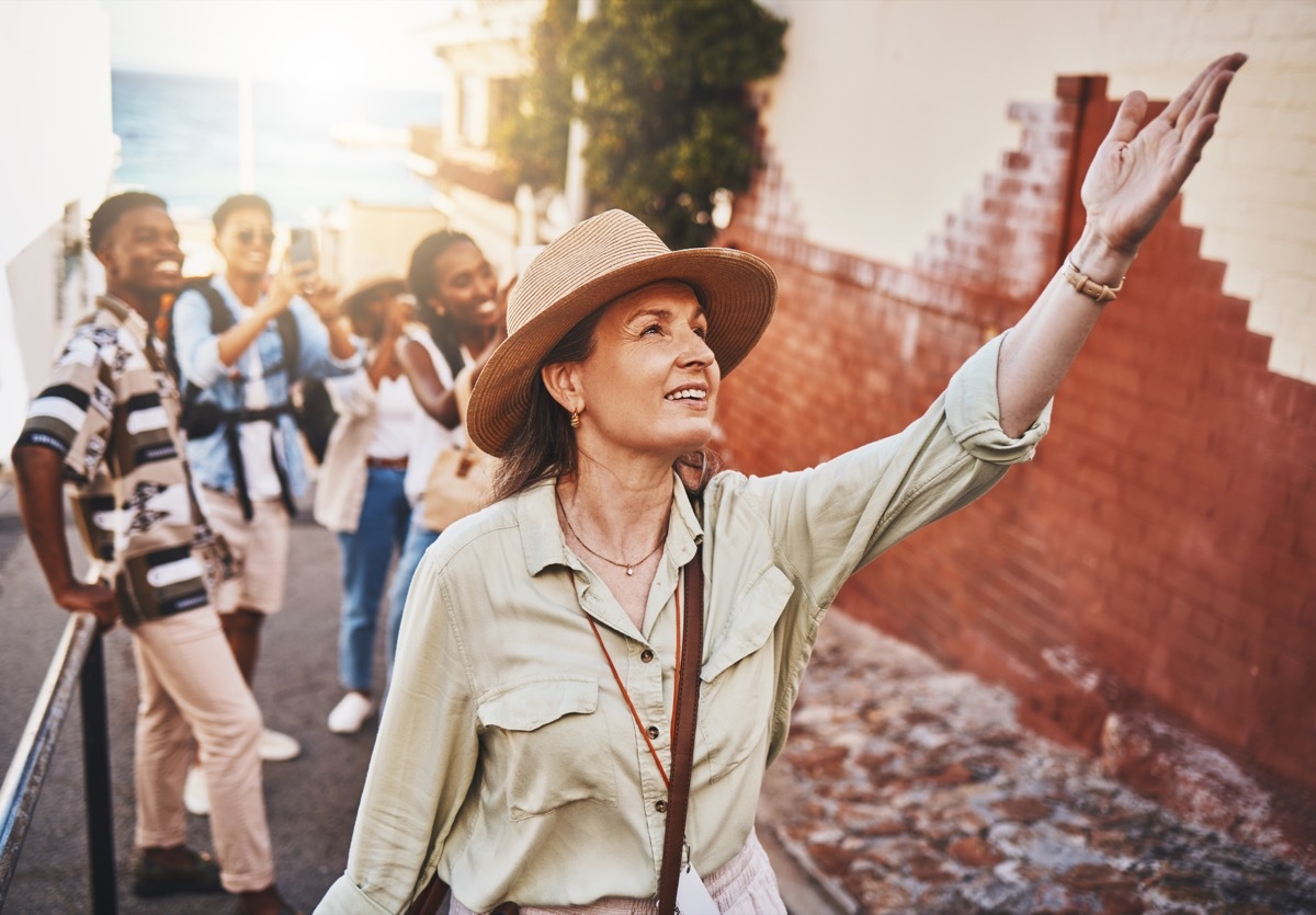 Travel, education and a teacher with students on school field trip, on urban tour. Woman, city guide and group of happy tourists, pointing at local architecture and learning on international holiday