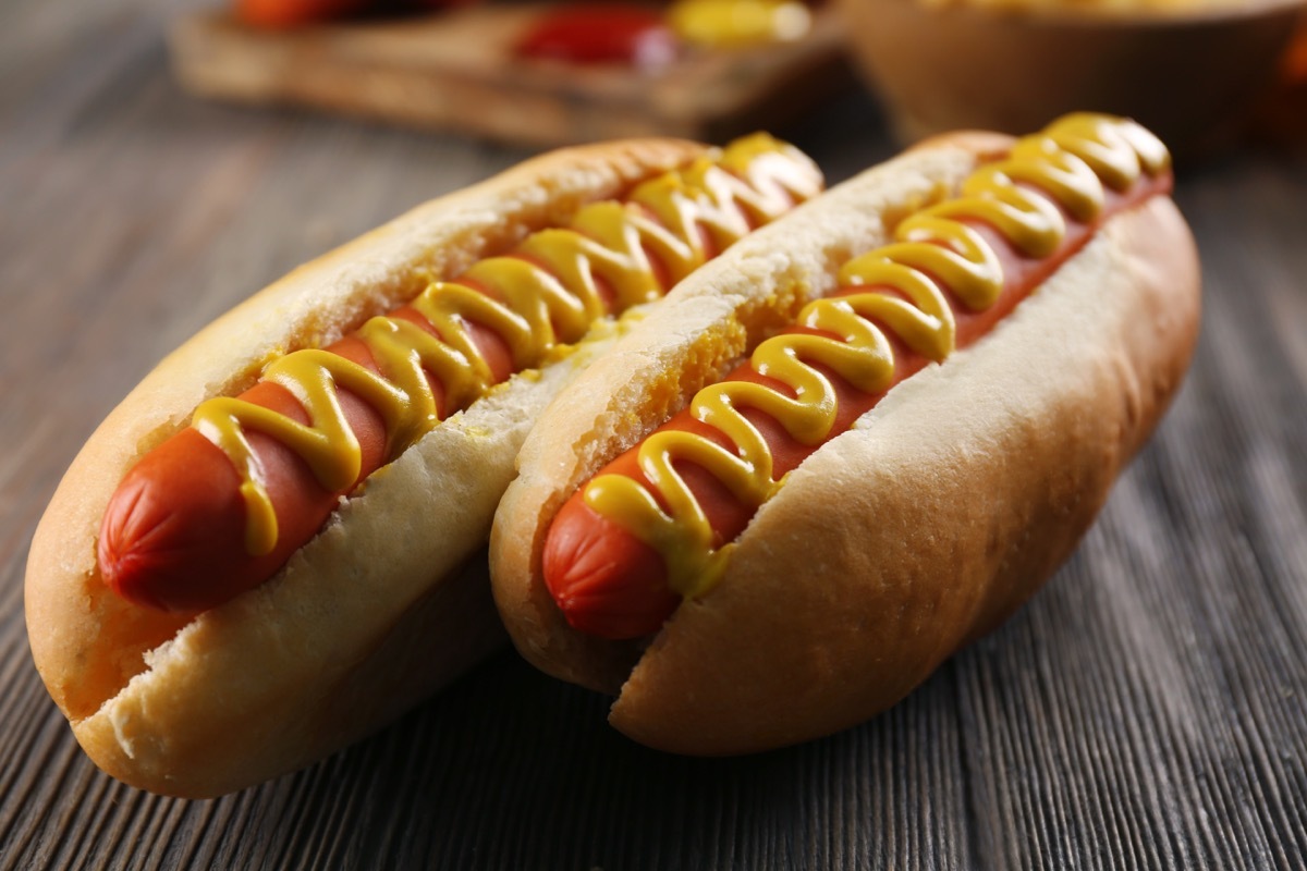 two hot dogs in a bun, with mustard, wooden table