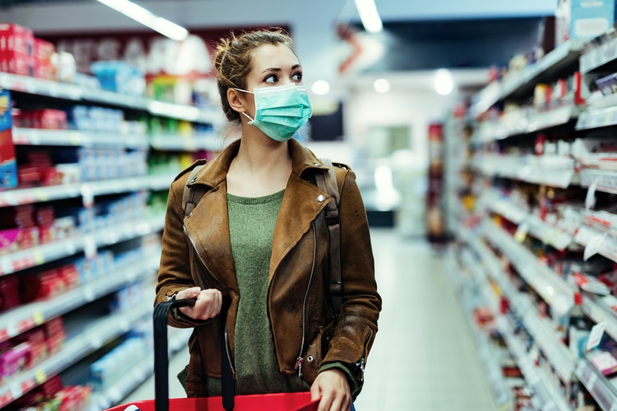 Young woman with face mask walking through grocery store during COVID-19 pandemic.