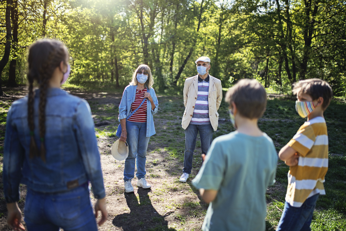 Grandparents and grandchildren meeting in the park with keeping distance and wearing masks.