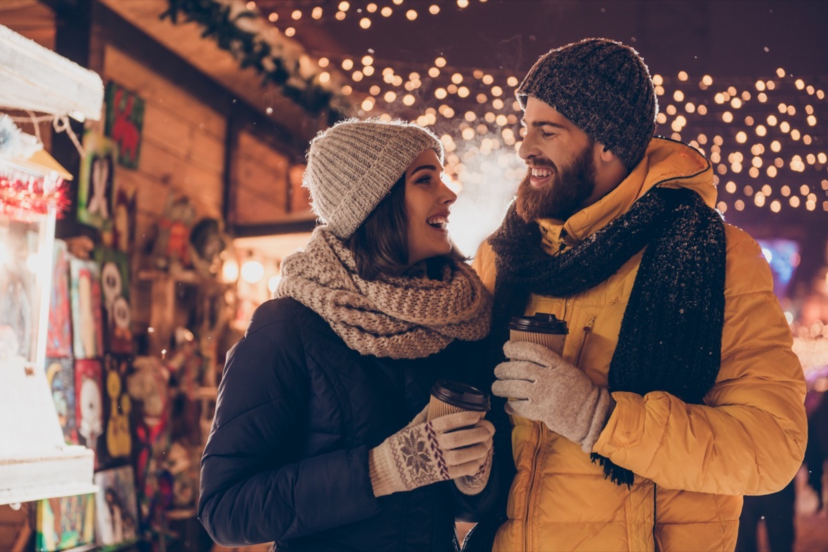 Man and woman drinking hot chocolate and walking through Christmas market