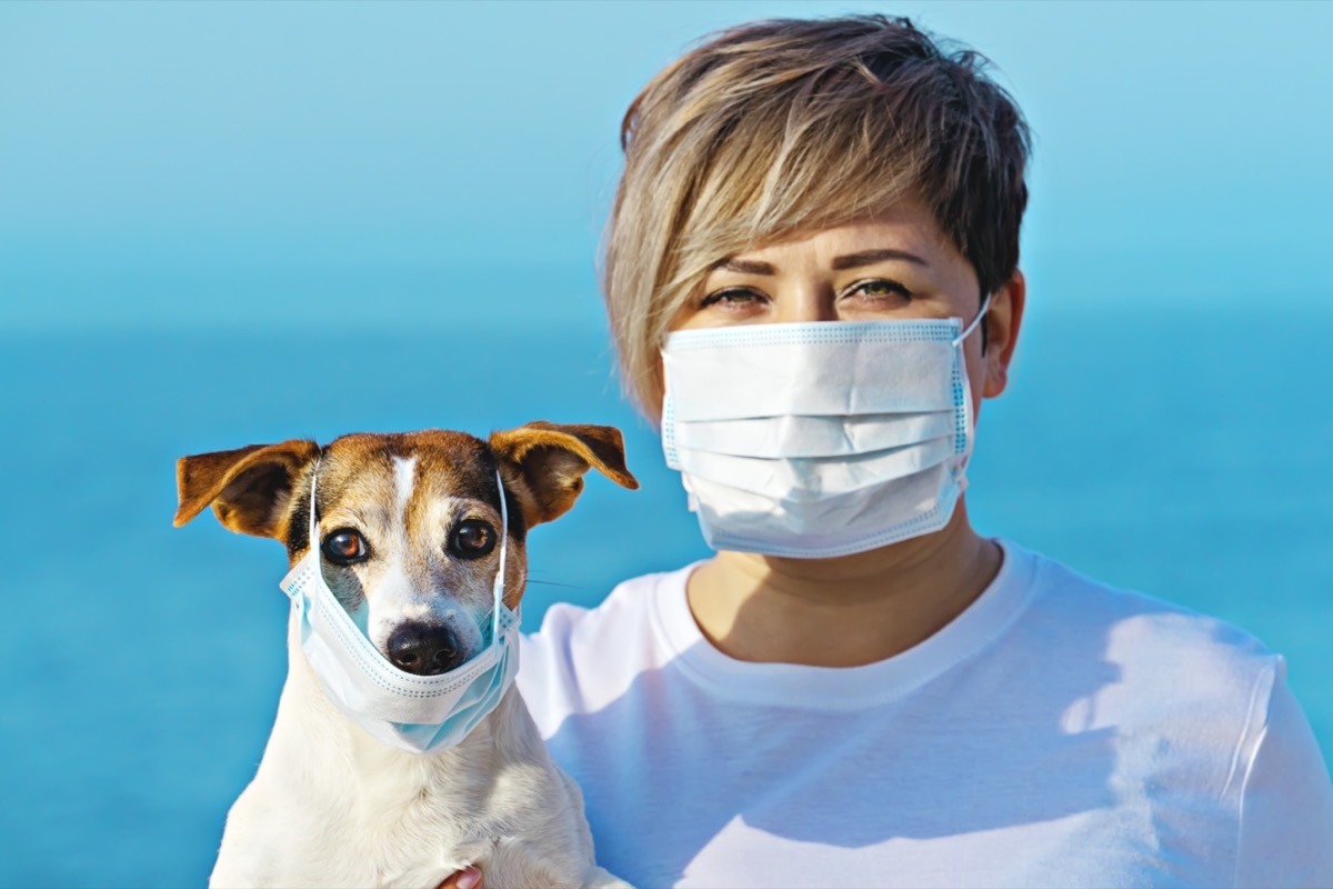 Woman in protective surgical mask holds dog pet in face mask