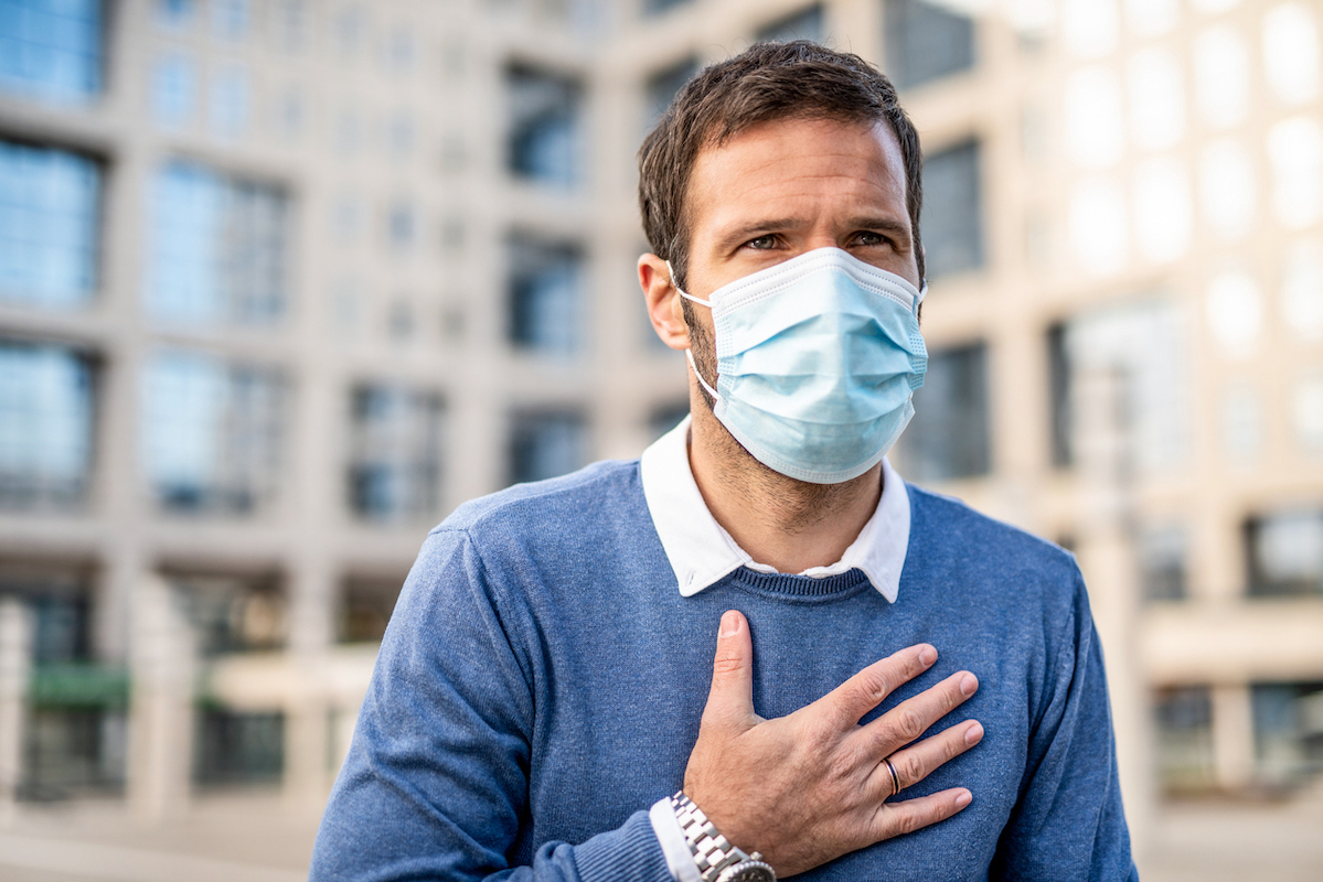 Mid adult man having health issues. Holding his chest and wearing a protection mask.