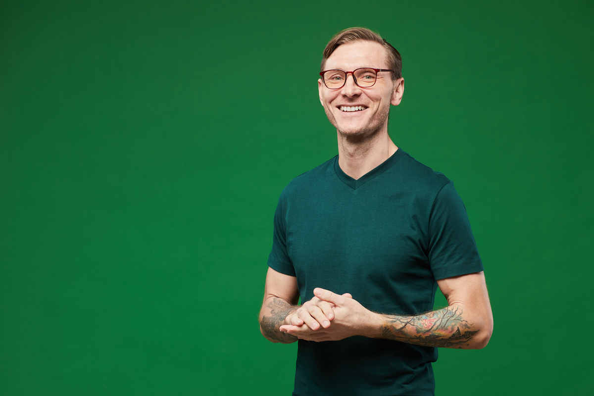 Waist up portrait of tattooed man wearing green shirt and glasses against vibrant green background