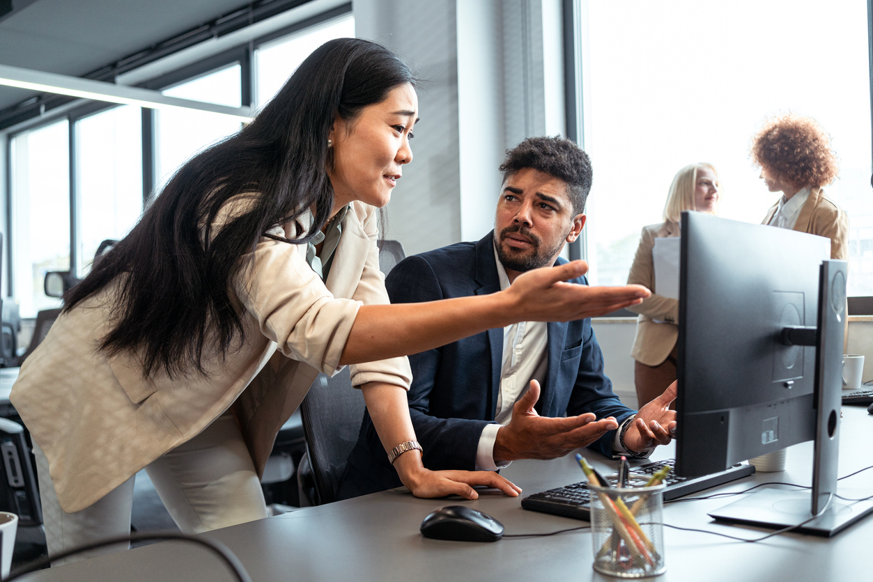 A disappointed female boss pointing to her male employee's computer screen