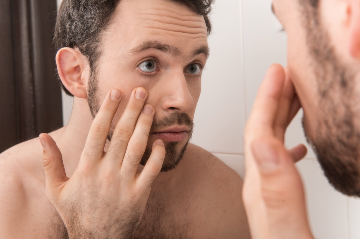 young man looking at his eye in the mirror