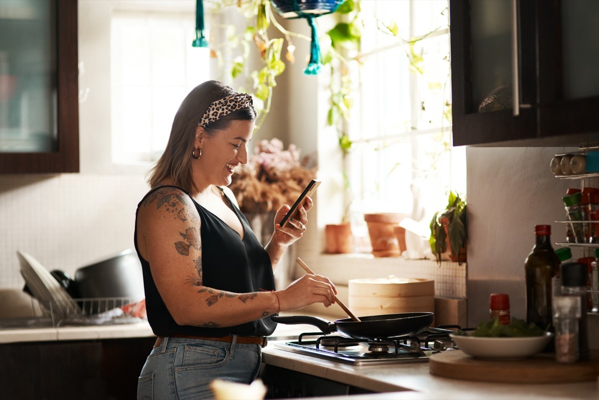 Shot of a young woman using a smartphone while preparing a meal at home