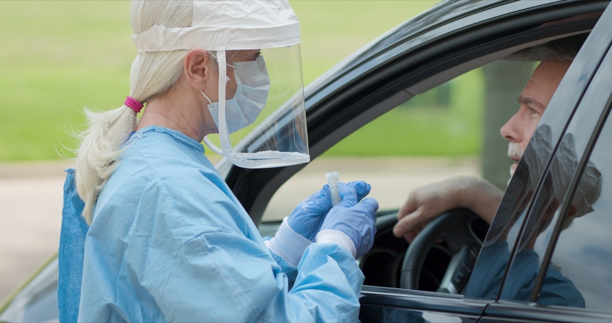 Dressed in full protective gear a healthcare worker collects a sample from a mature man sitting inside his car as part of the operations of a coronavirus mobile testing unit.