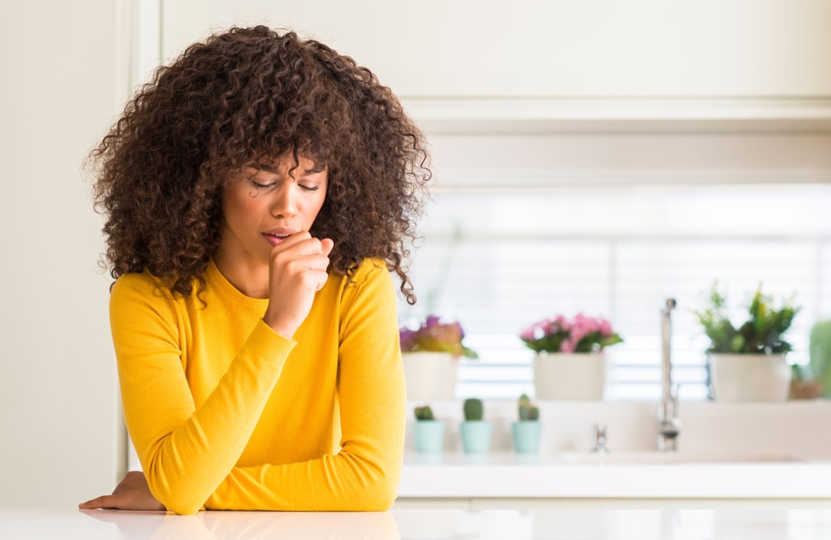 woman wearing yellow sweater at kitchen feeling unwell and coughing as symptom for cold or bronchitis