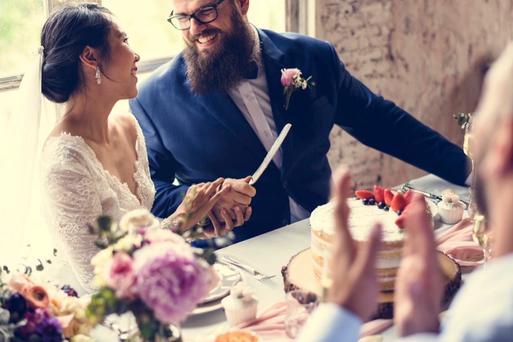 asian bride and white groom cut wedding cake 