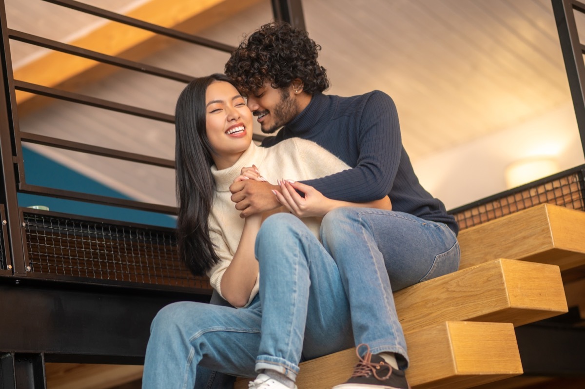 Man hugging his girlfriend on the stairs while whispering in her ear