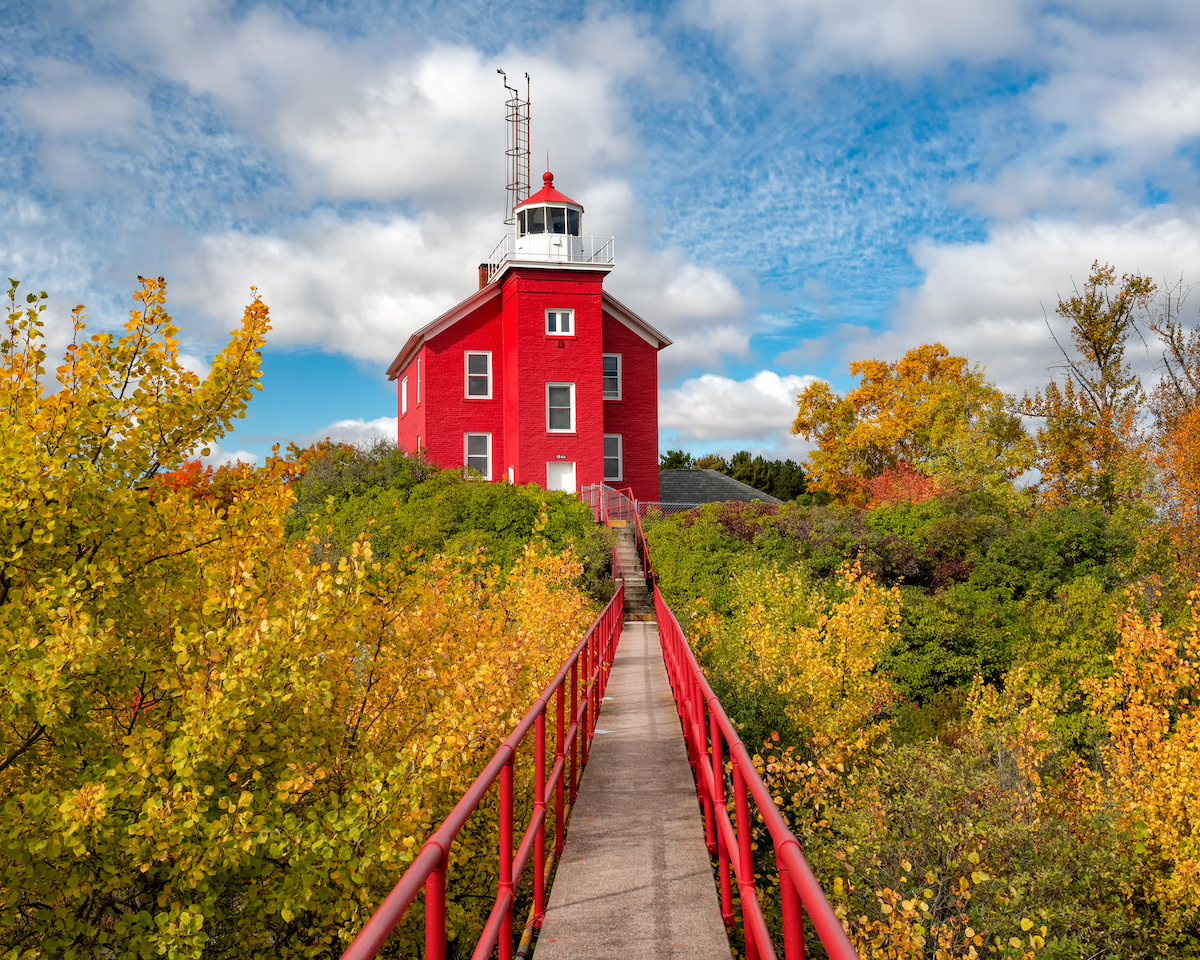 The bright red Marquette Harbor Lighthouse in Michigan with fall colors surrounding it.