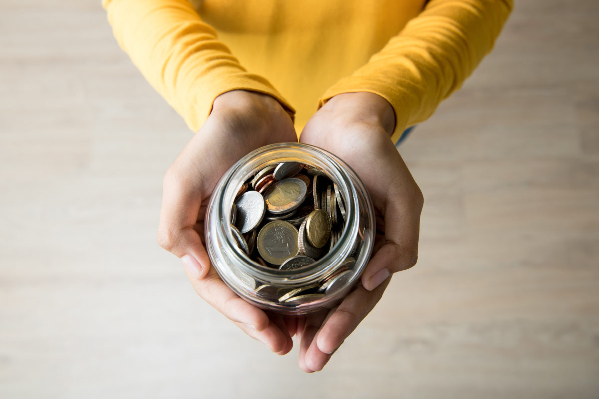 person's hands holding out a jar of change