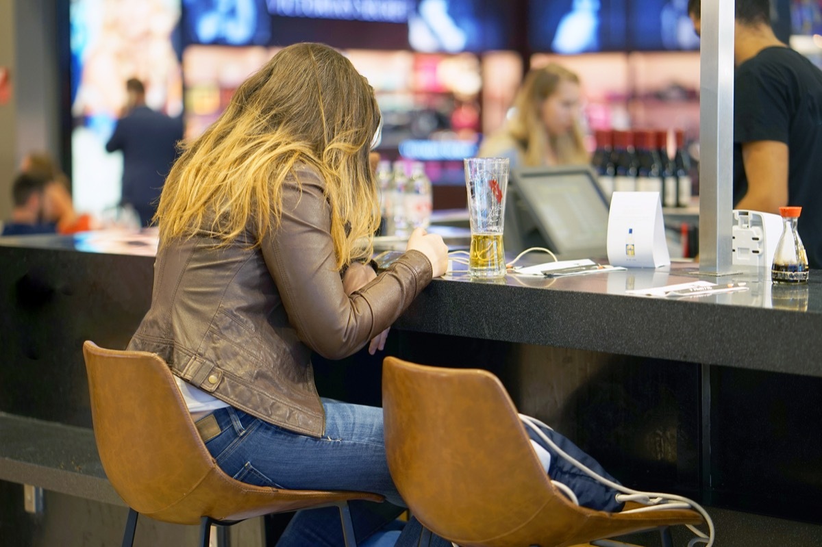 A girl drinks beer in the airport's cafe-bar and waits for her flight. A girl drinks beer in a cafe and looks into the phone.