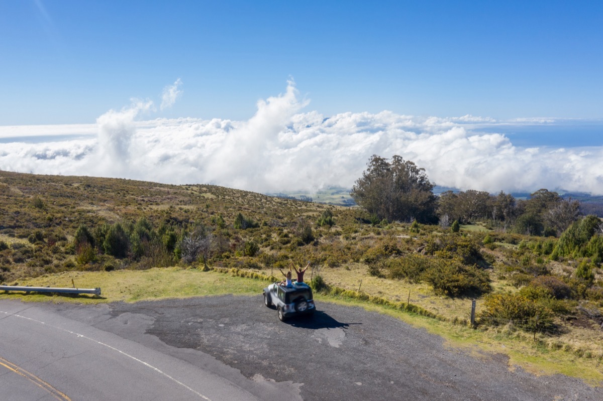 Young couple sitting on vehicle roof looking at cloudscape in Hawaii, USA