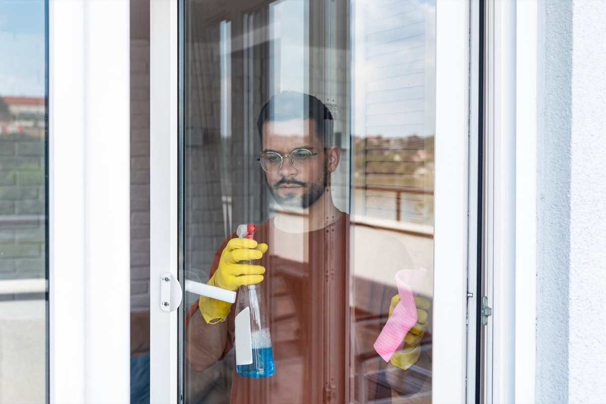 man wearing robber gloves and spray sliding door glass to clean at house