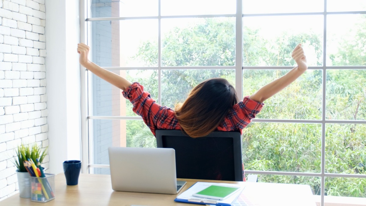 Woman in a plaid shirt stretching at work. 