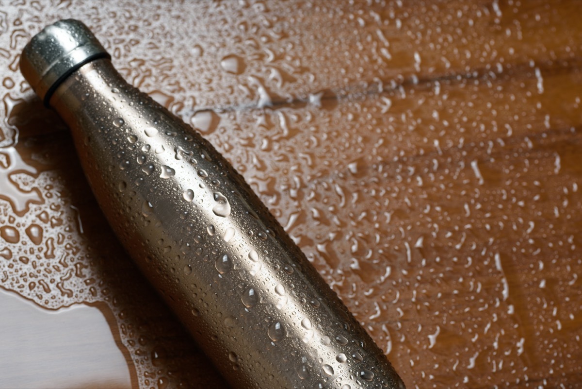 Stainless thermos bottle on a wooden table sprayed with water