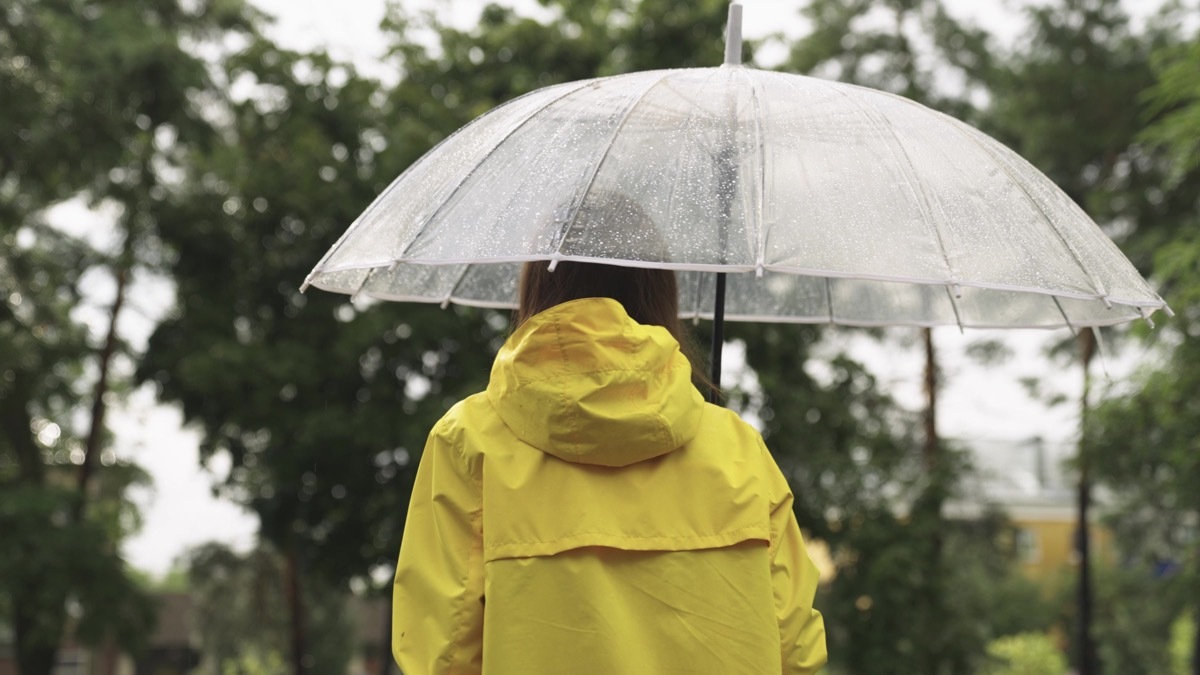 girl under umbrella. Slow motion. rain city park. view from back. young woman hiding under umbrella from raindrops. walk slush. rainfall rain. bad cloudy weather. man walks through wet streets park