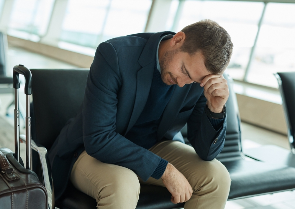 A man sitting in the airport with his head in his hands looking disappointed