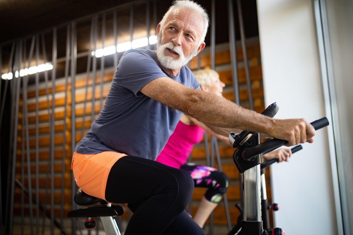 Mature fit people biking in the gym, exercising legs doing cardio workout cycling bikes