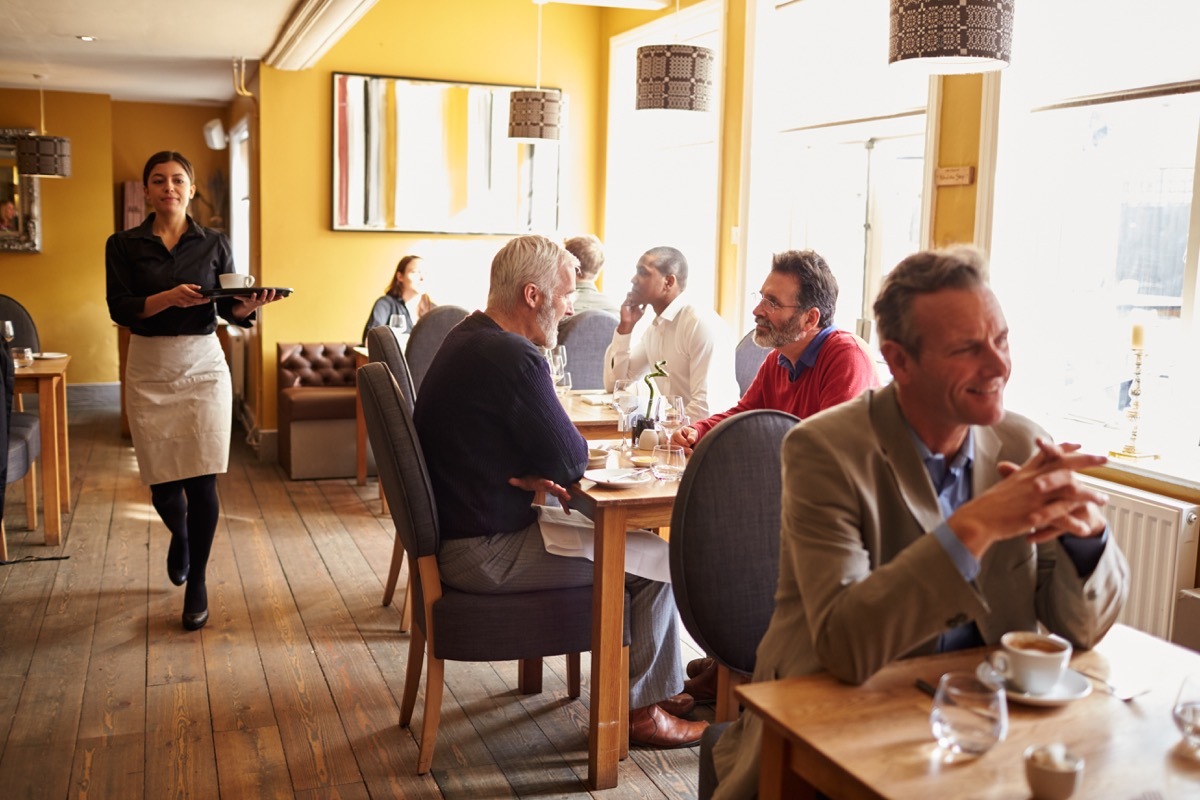 Customers at tables and waitress in busy restaurant interior