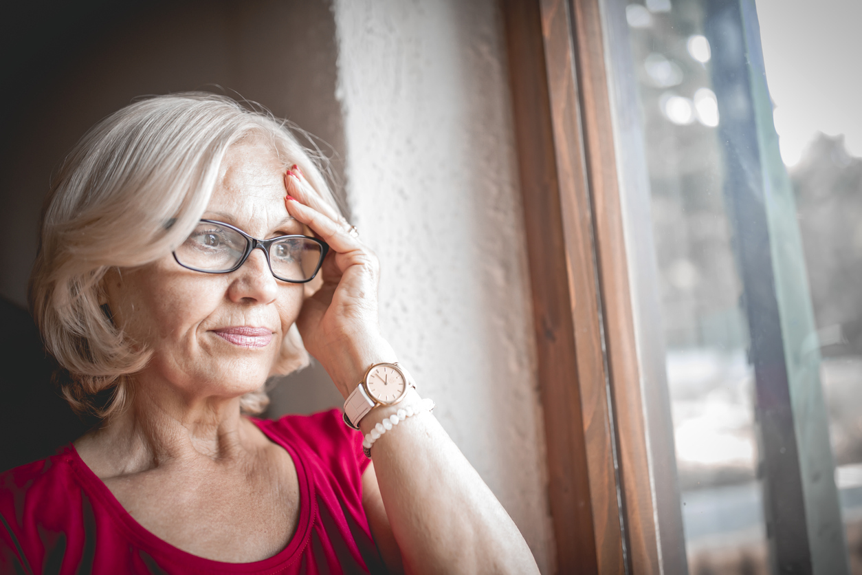 Woman looking out of window with her hand to her head.