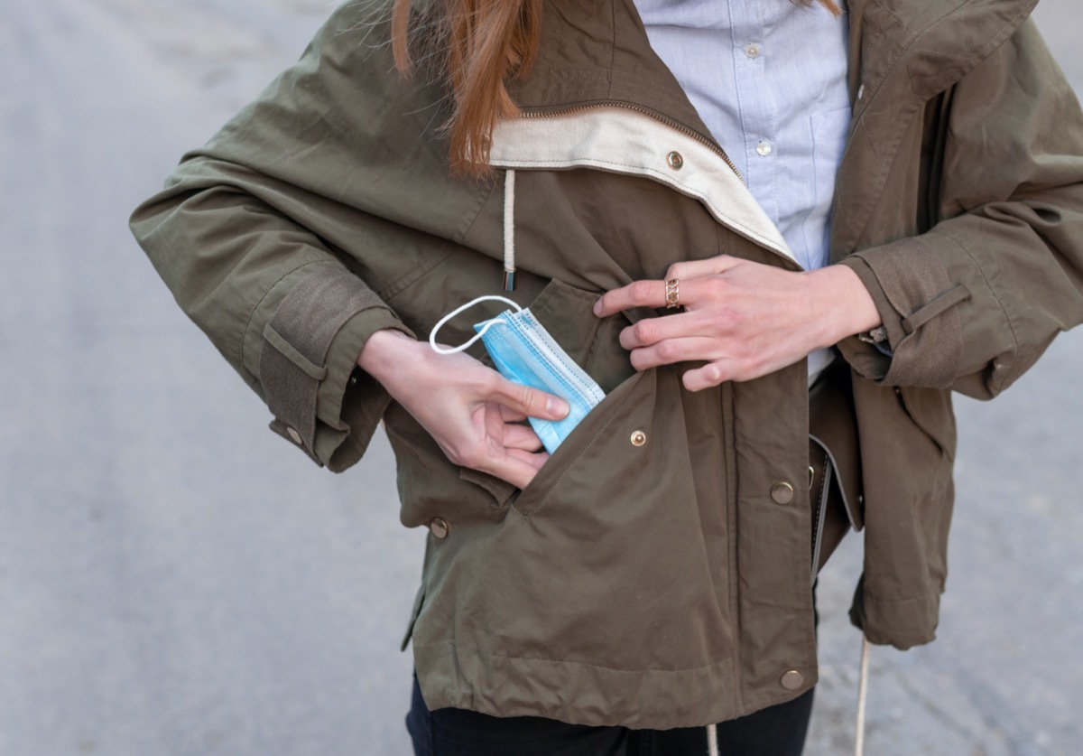 girl's hands pulling surgical protective face mask out of her green pocket,